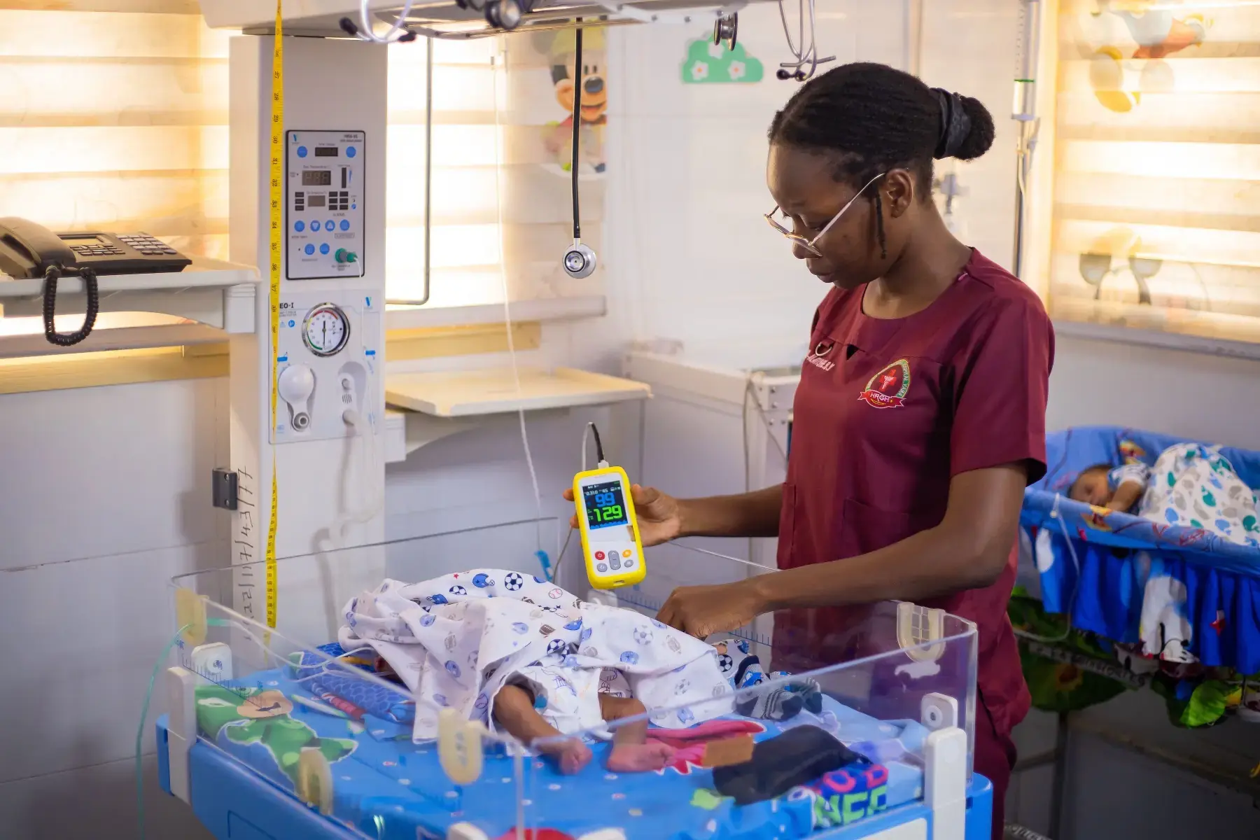 Neonatal nurse reading a pulse oximeter beside an incubator